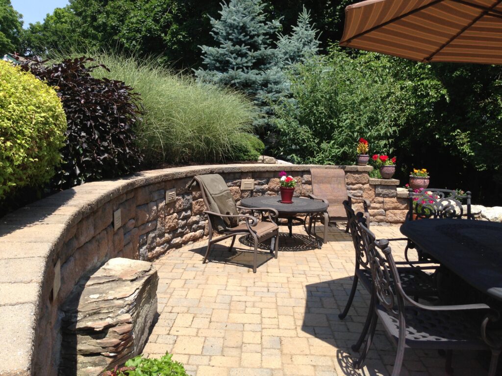 Landscaped outdoor living space. Paver patio with retaining wall with boulders in Barto