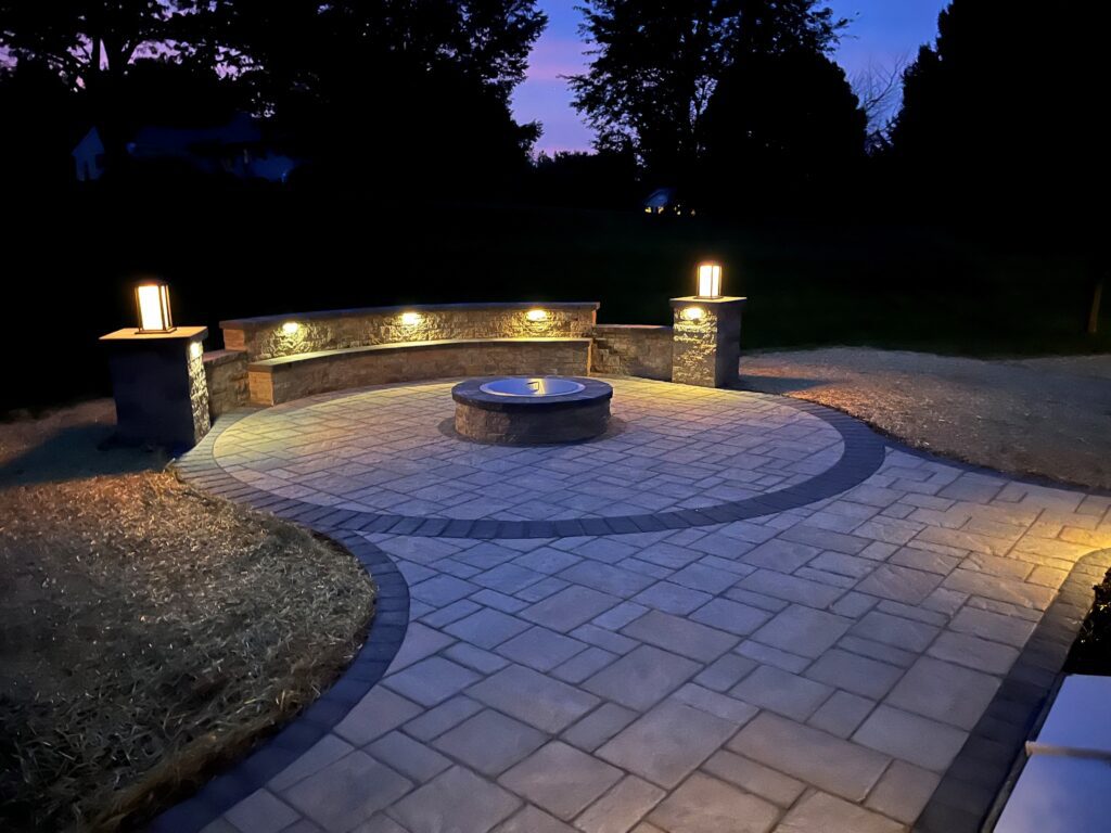 Round patio with sitting wall, lighting and firepit in Gilbertsville